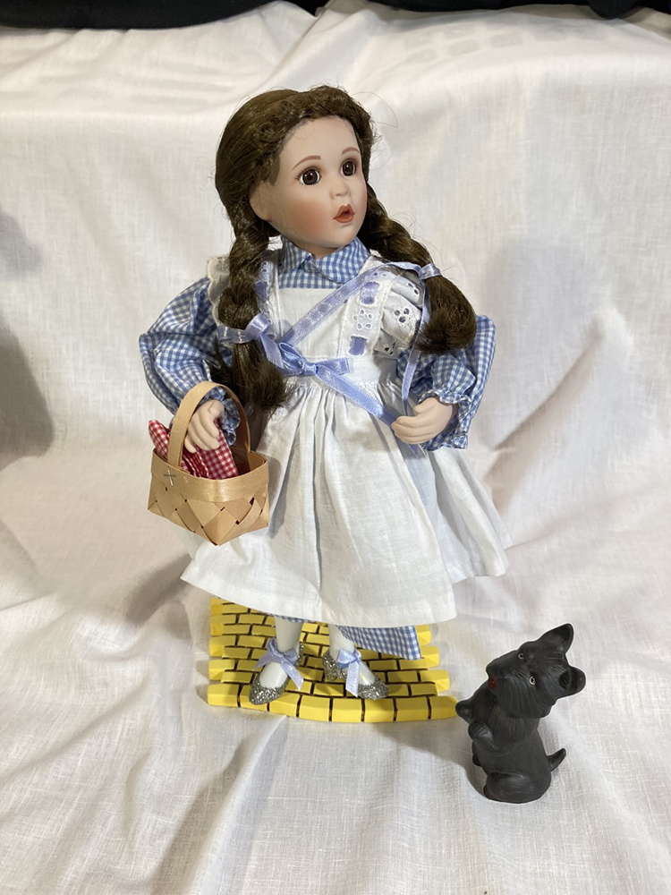 Collectible Wizard of Oz Dorothy porcelain doll on yellow brick road stand; doll stands 14.5″ tall with Toto and small basket